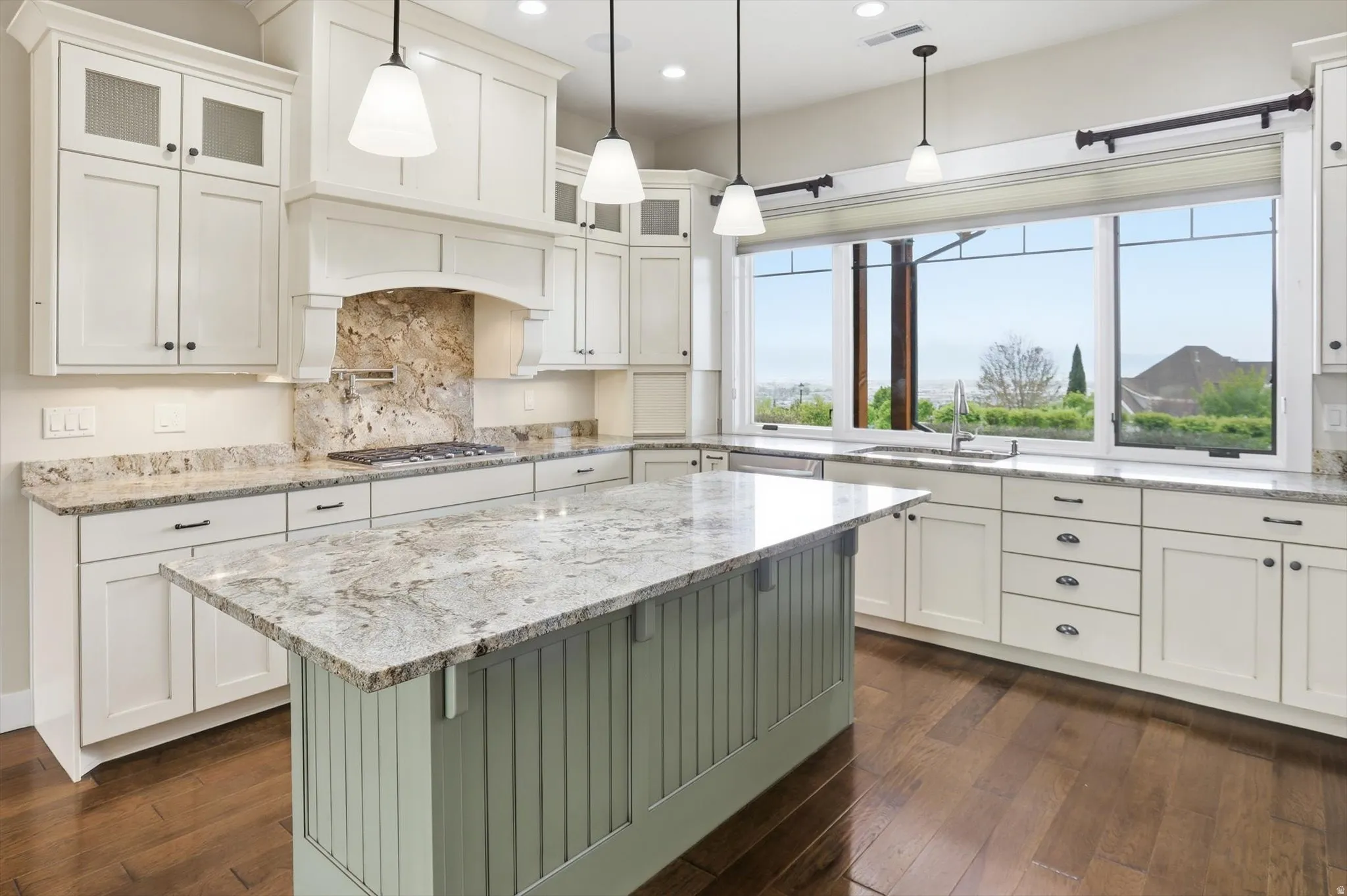 Kitchen featuring a light-toned island with beadboard paneling, extensive cabinetry with dark hardware, stone countertops, and a full-height stone backsplash