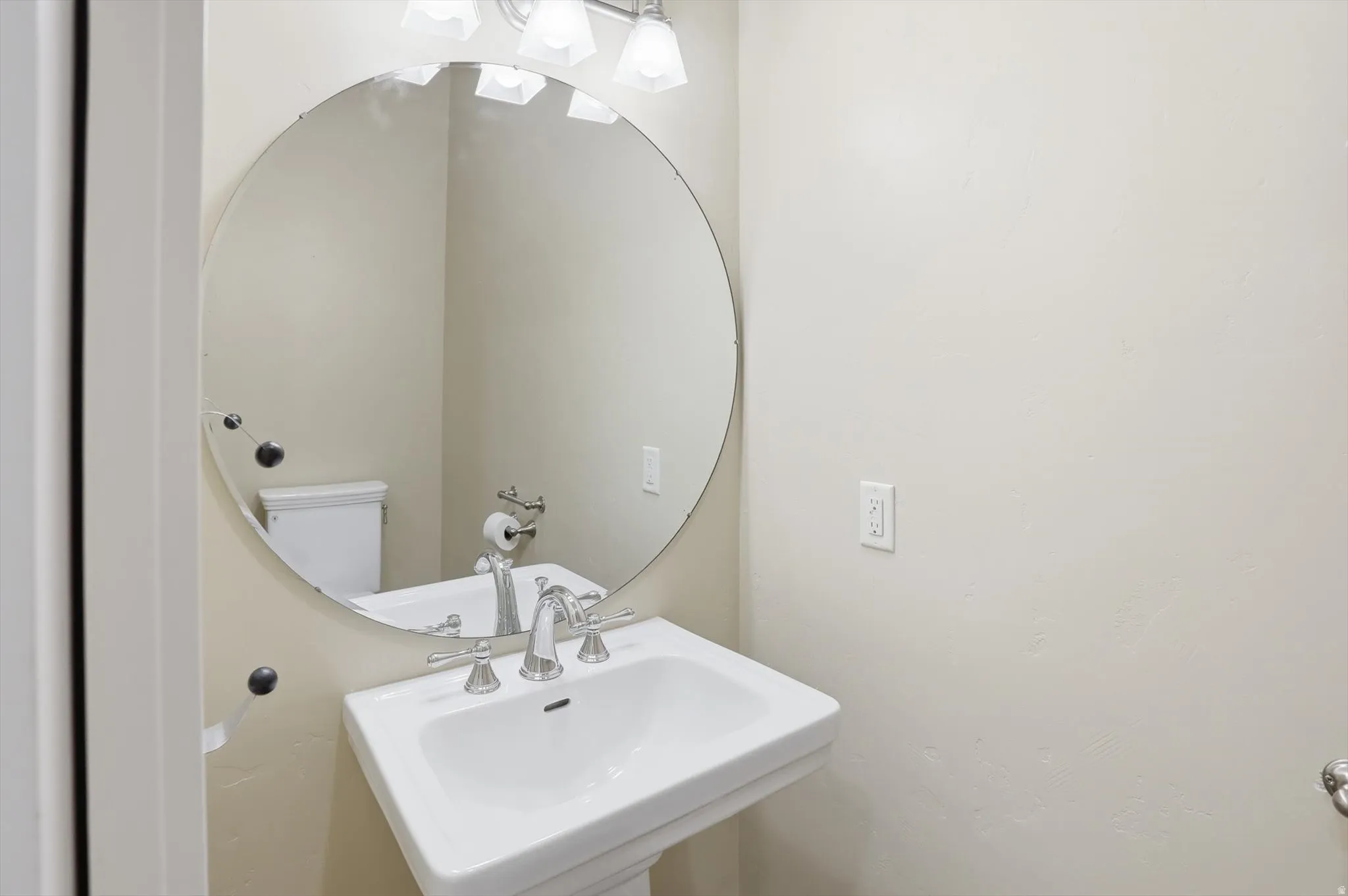 Pedestal sink with chrome fixtures and a circular mirror