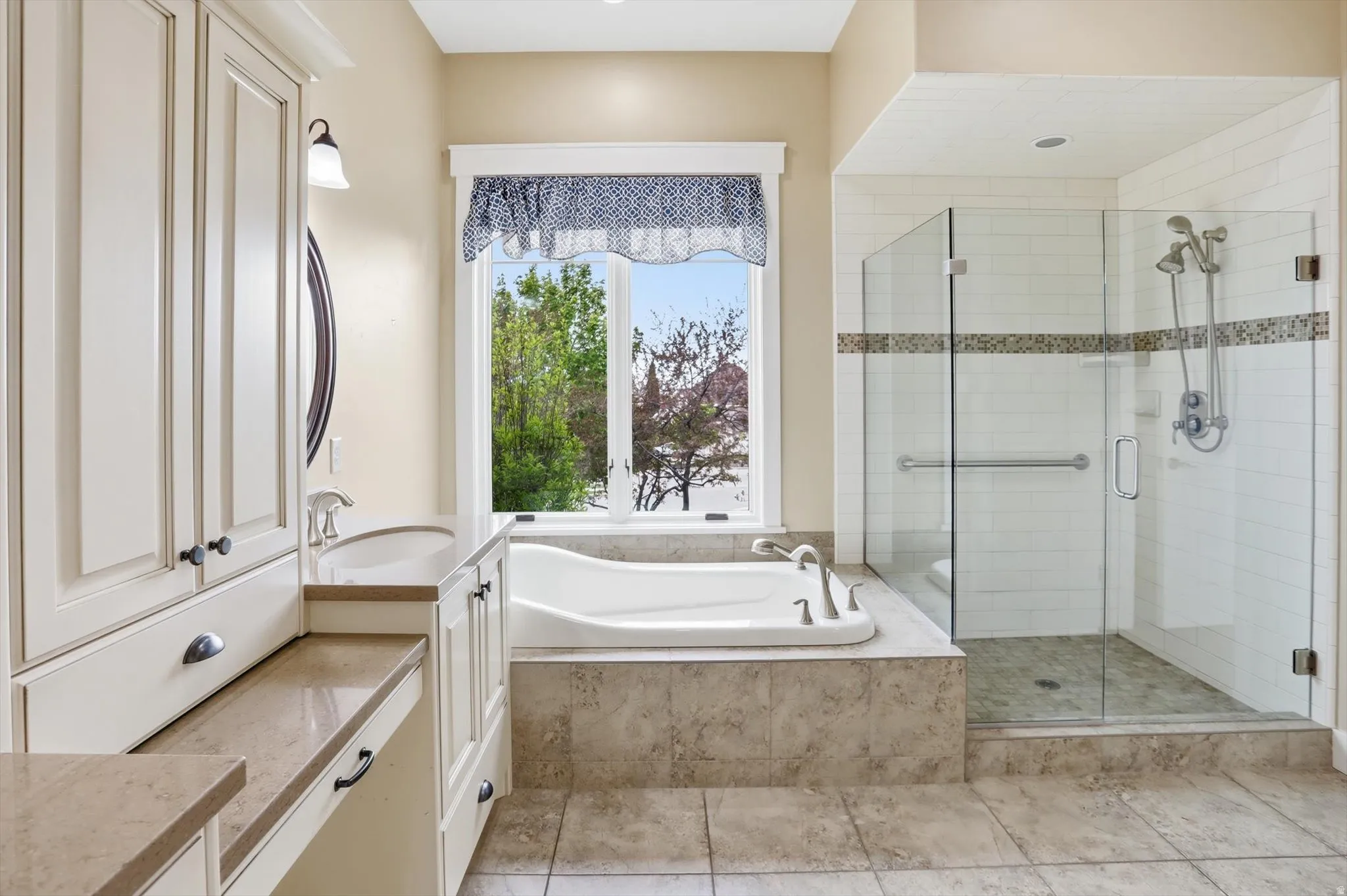 Spacious bathroom featuring a built-in soaking tub, a walk-in glass-enclosed shower, extensive cabinetry, and neutral-toned tile flooring
