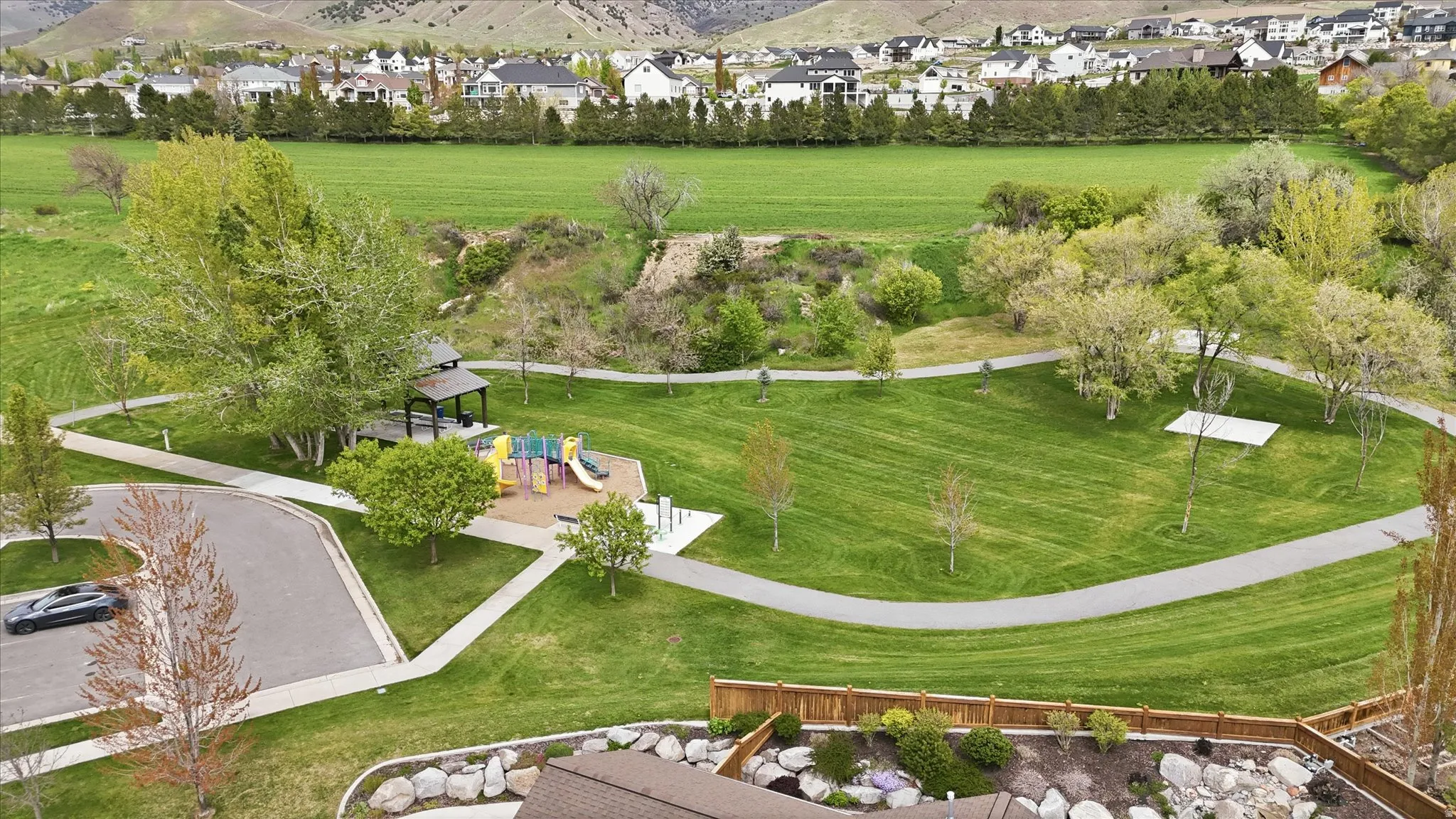Expansive park area featuring a playground, paved walking paths, a covered gazebo, and mature trees