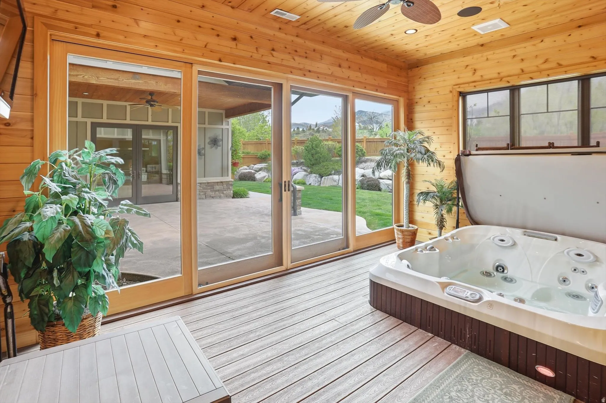 Enclosed sunroom featuring a built-in hot tub, wood-panel walls and ceiling, wood-finish flooring, and large sliding glass doors opening to the exterior patio