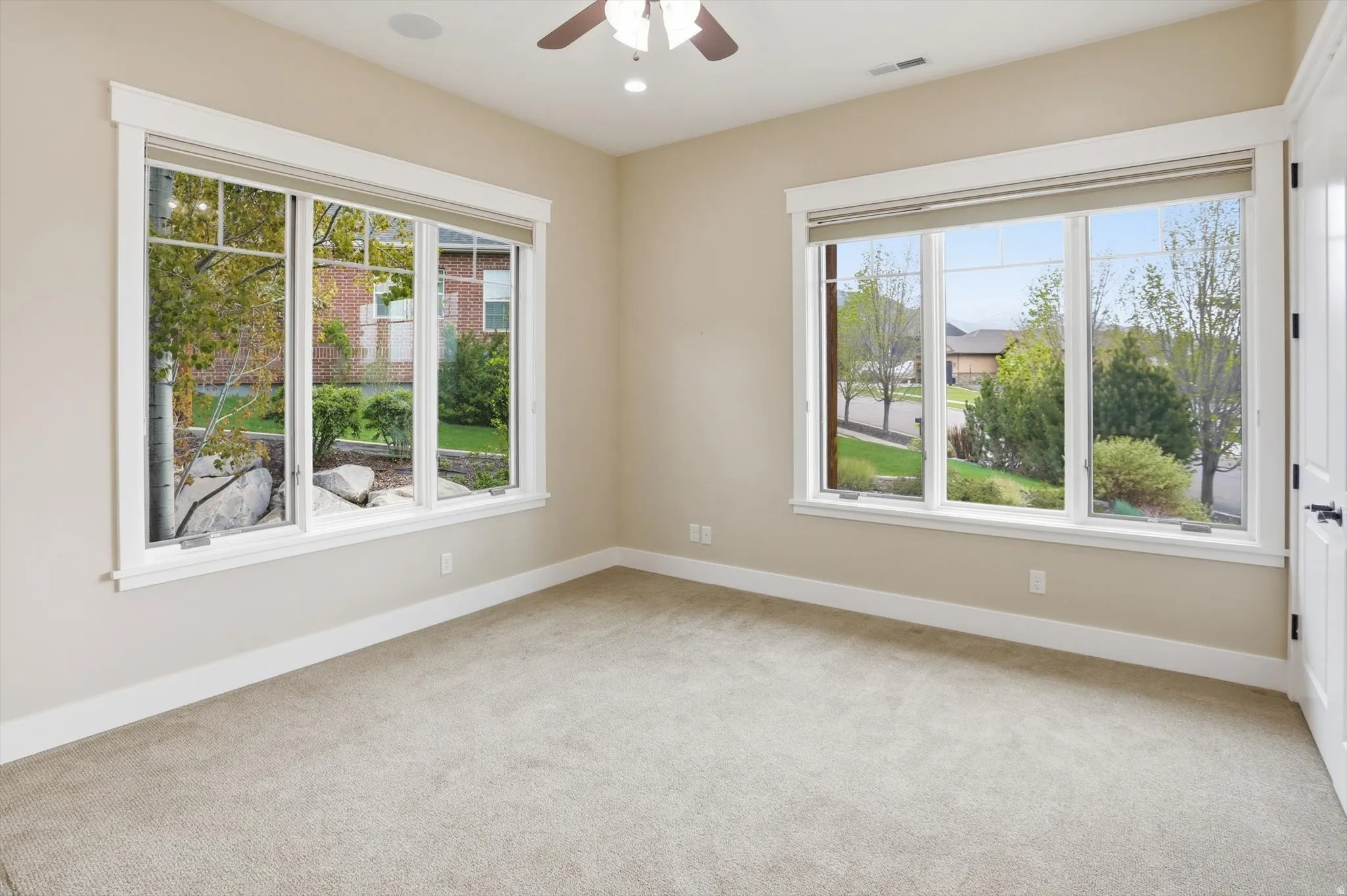 Spacious room featuring neutral carpeting, light beige wall paint, white trim, and a ceiling fan