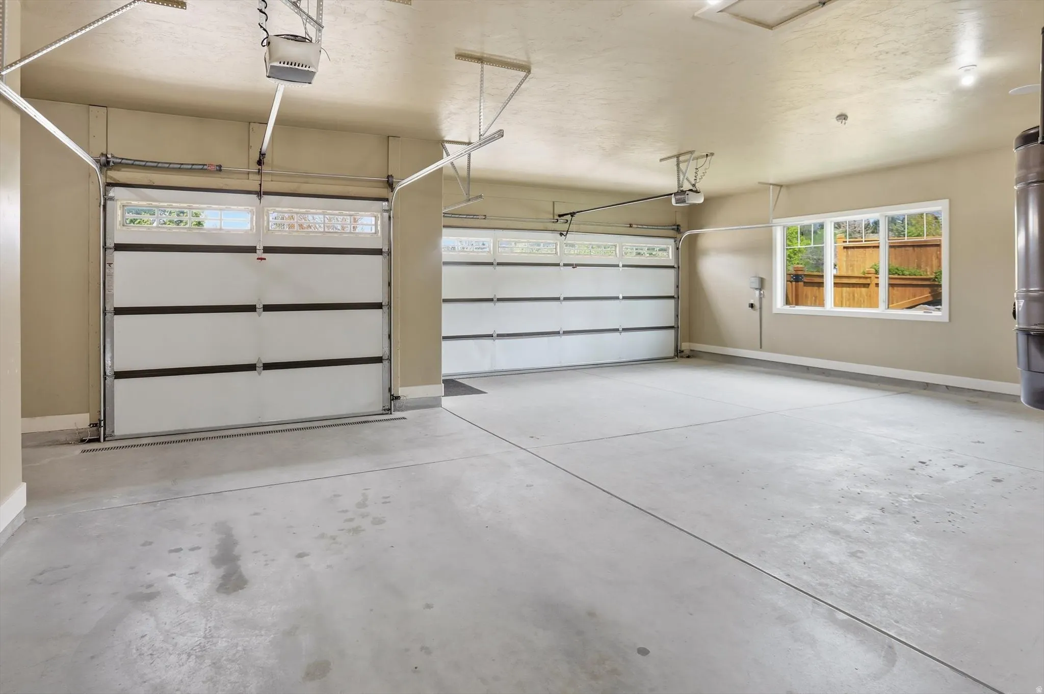 Spacious heated garage featuring two overhead doors with frosted glass panels, an automatic door opener, concrete flooring, painted walls, and a large window
