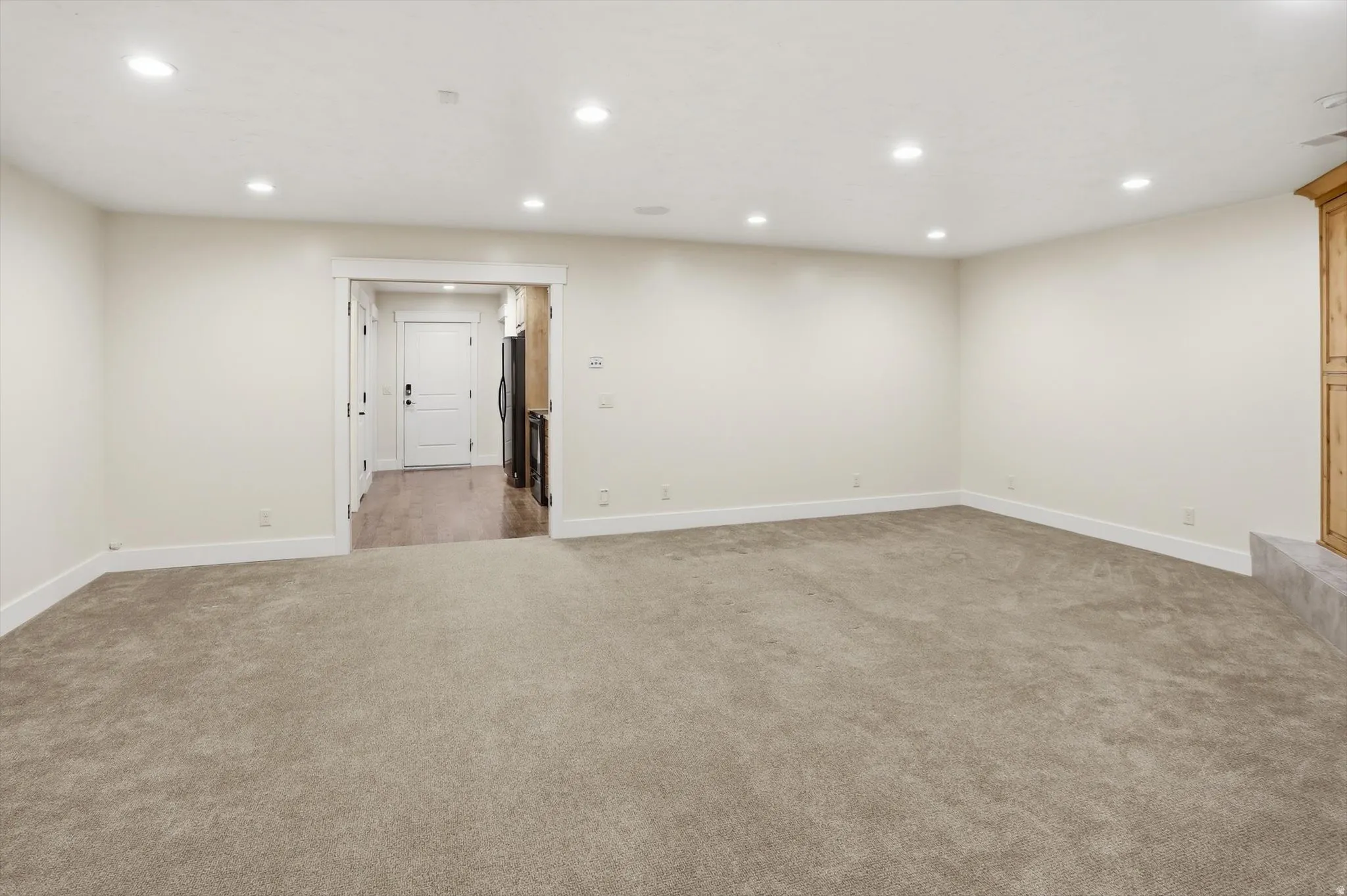 Spacious room featuring neutral carpeting, recessed lighting, white baseboards, and a doorway leading to wood-finish flooring