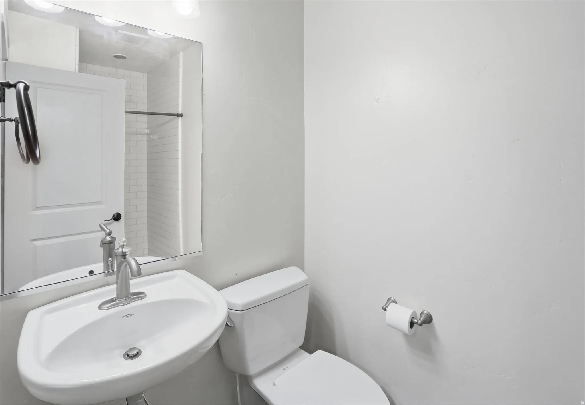 Pedestal sink with brushed nickel faucet, mirror, and two-bulb vanity light fixture