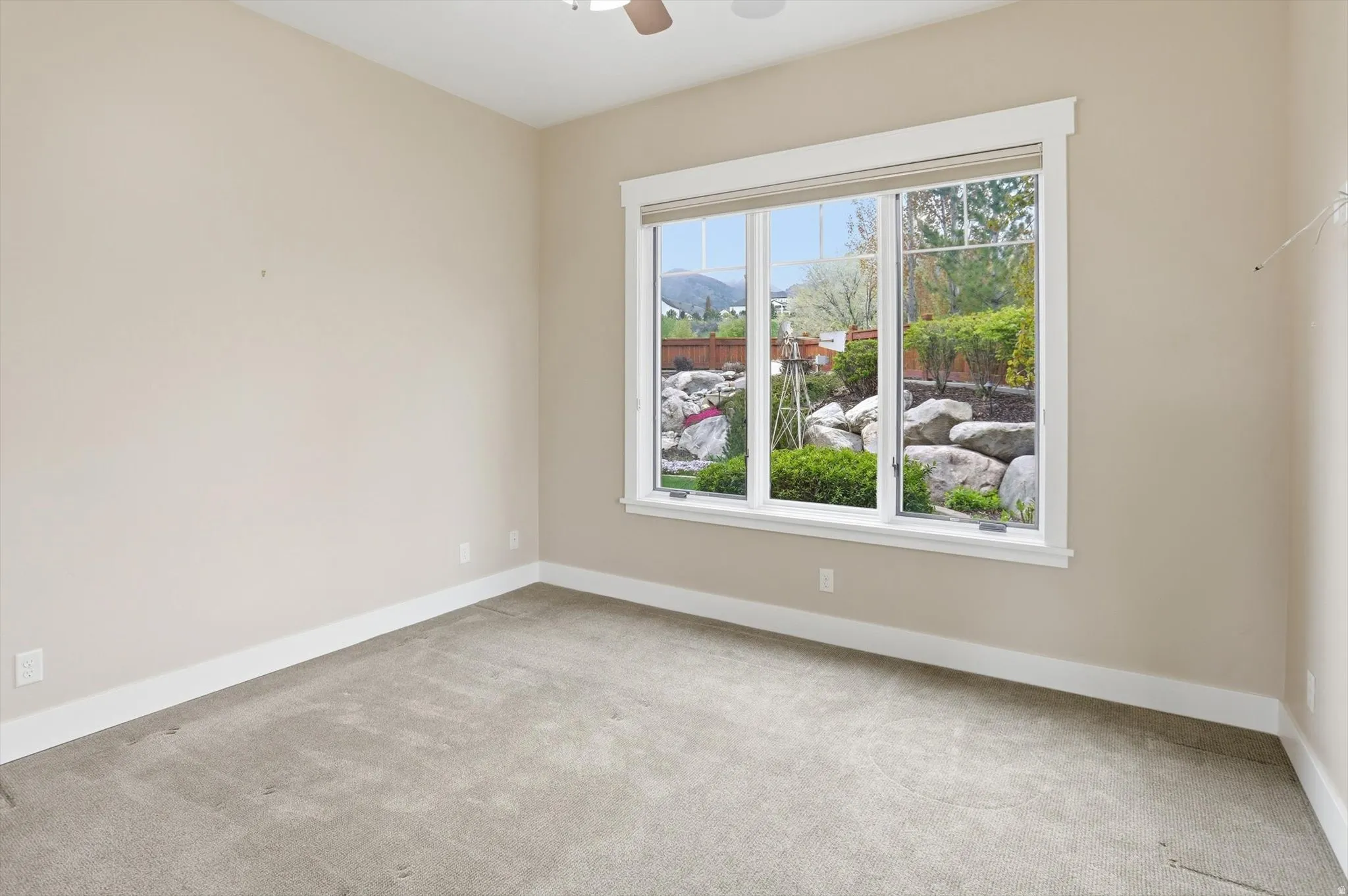 Neutral-toned room featuring a large window with white trim, carpeting, and a ceiling fan