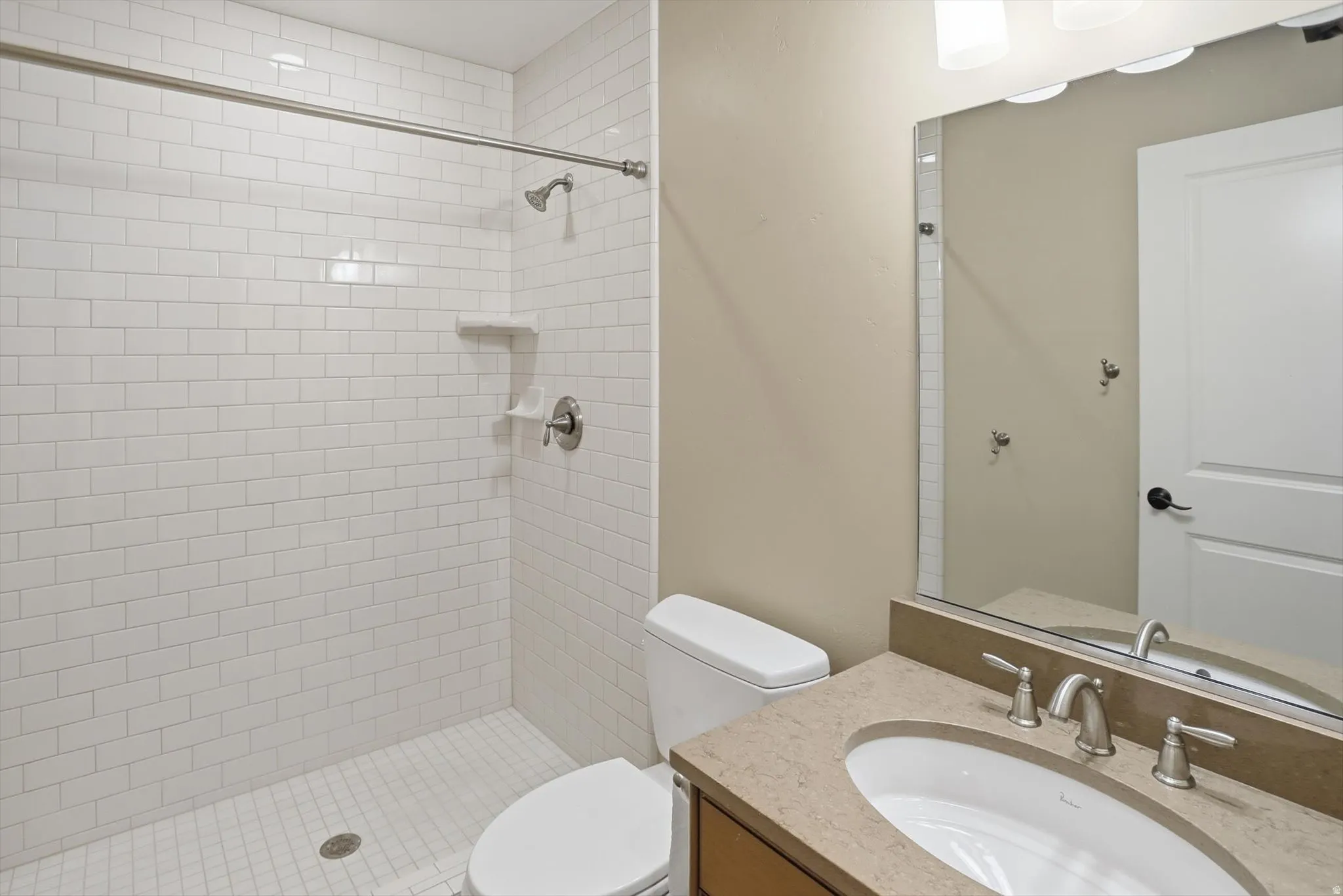 Bathroom featuring a subway-tiled shower with a built-in shelf, a brushed nickel showerhead and faucet, and a tiled shower pan