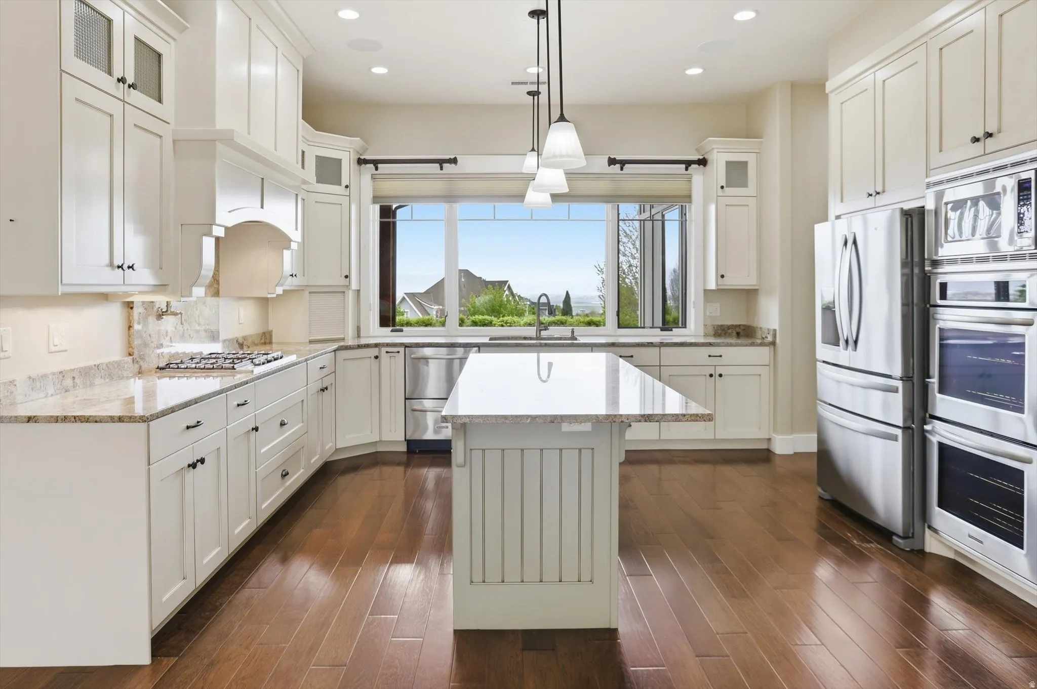 Bright kitchen with wood-finish flooring, white cabinetry, integrated stainless steel appliances, a center island with a light-toned countertop, and perimeter countertops with a coordinating backsplash