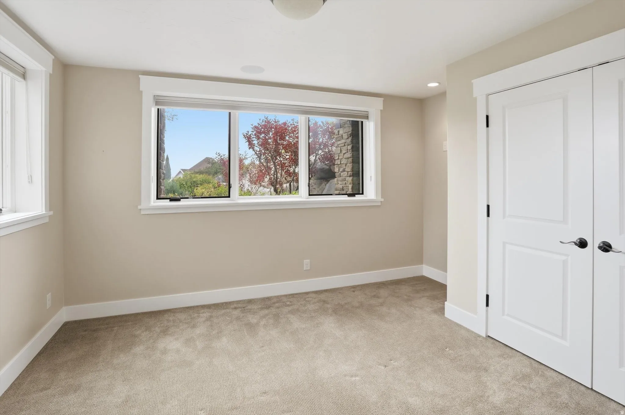 Carpeted room featuring multiple windows with white trim, two white bifold closet doors with dark hardware, and light-colored walls