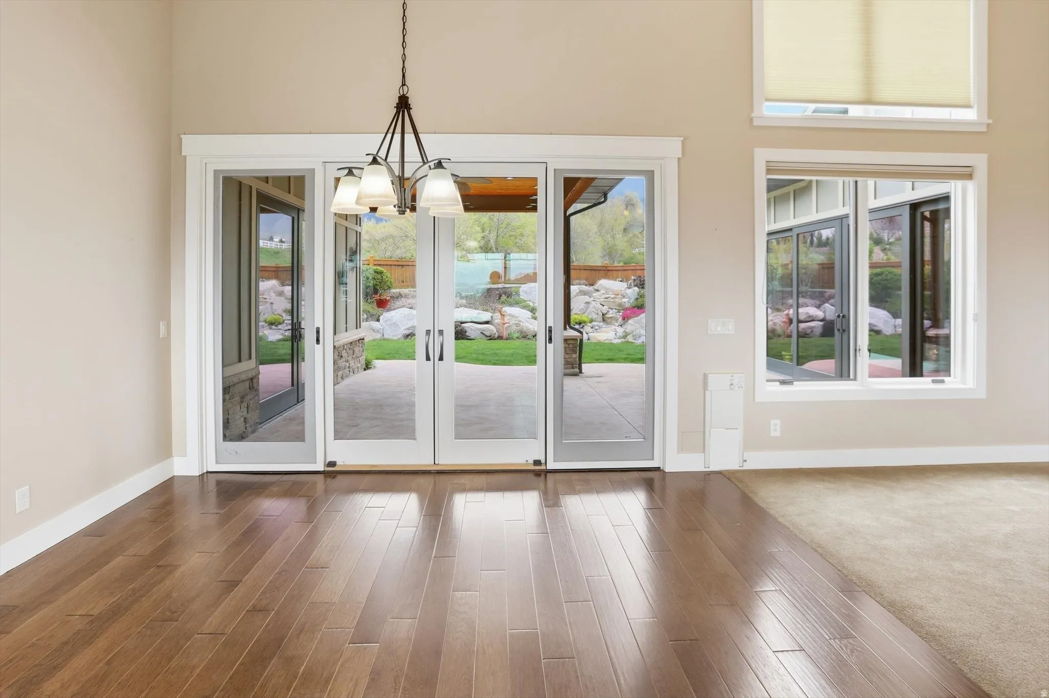 Open-concept interior featuring wood-finish flooring, a multi-pane glass door leading to a patio, and a chandelier with frosted glass shades