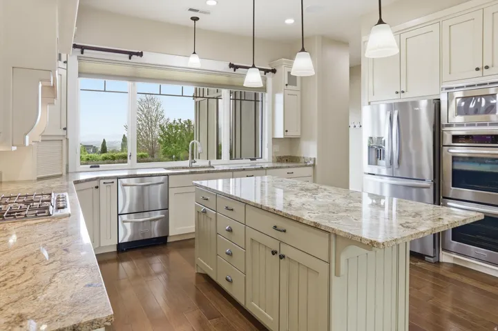 Light-toned cabinetry kitchen featuring a central island with a stone countertop, coordinating perimeter countertops, dark wood-finish flooring, and stainless steel appliances