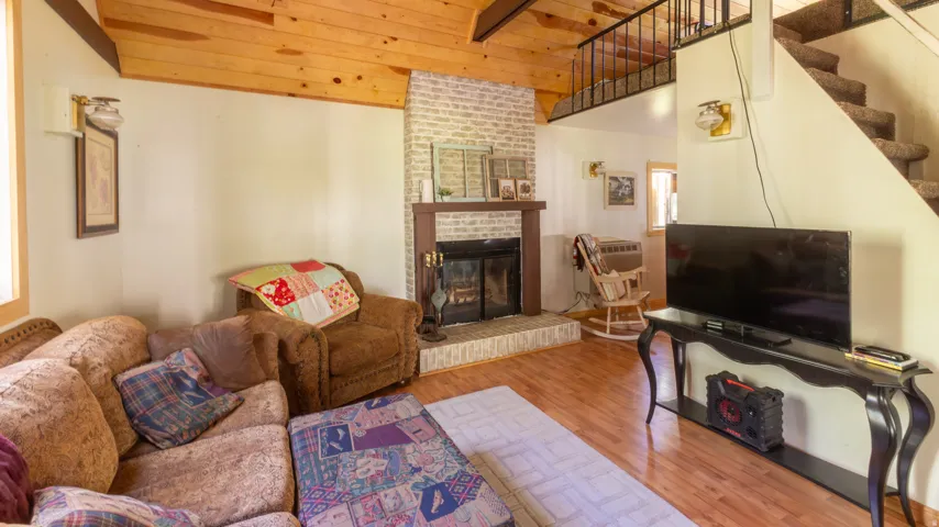 Living area featuring a brick fireplace, wood-finish flooring, vaulted wood-plank ceiling, and a carpeted staircase with an open railing