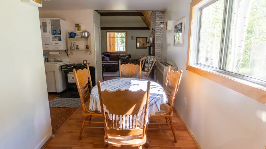 Dining area featuring a large window with natural wood trim, wood-finish flooring, and direct access to the kitchen
