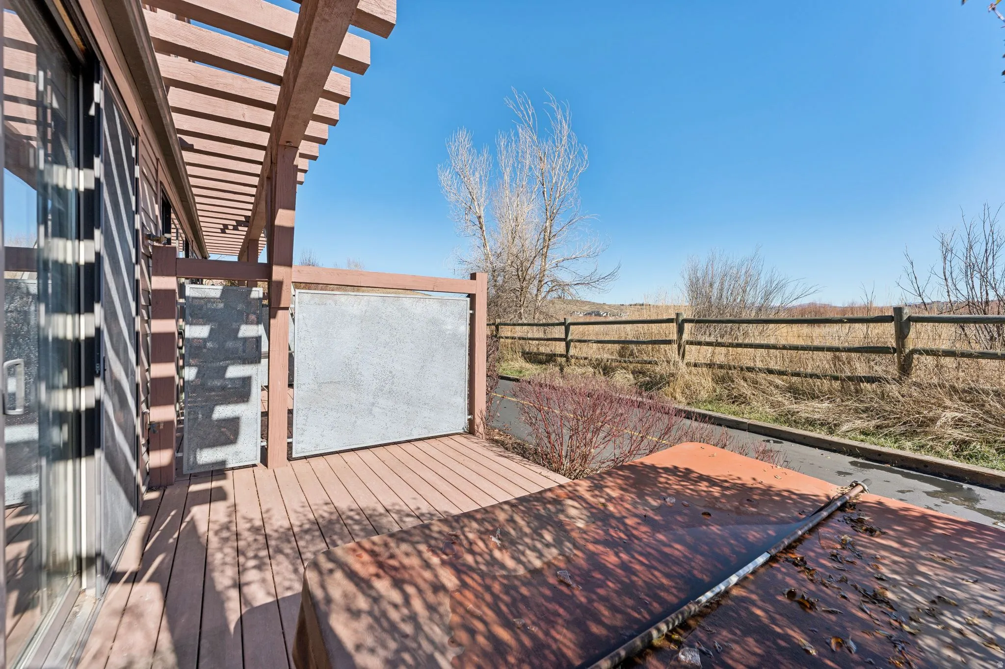 Composite decking area featuring a wooden pergola, sliding glass door, and a privacy screen