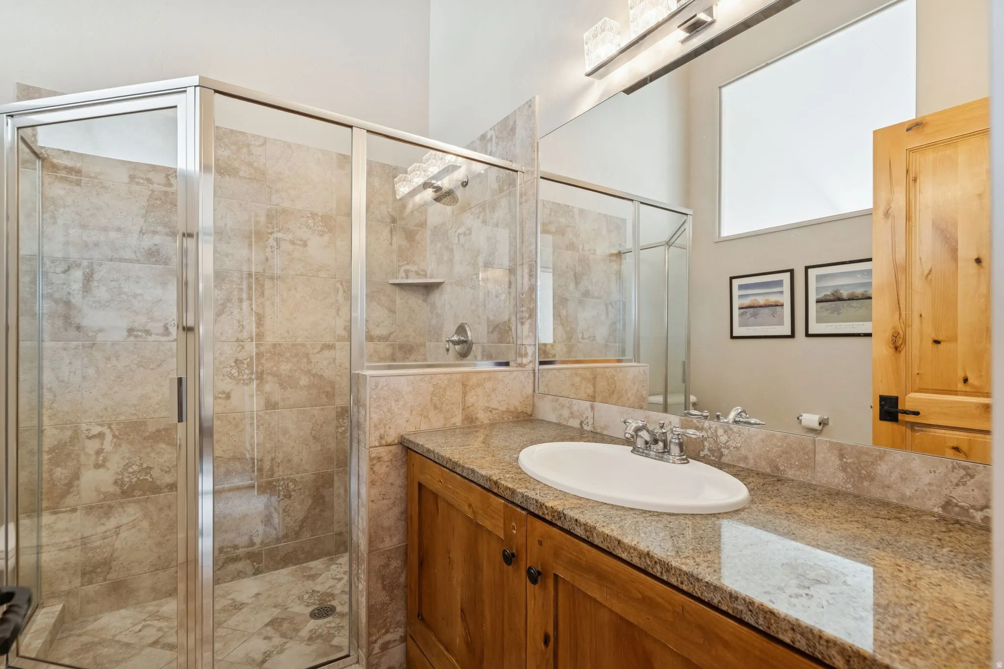 Bathroom featuring a glass-enclosed shower with full tile surround, a wood vanity with a stone countertop, an oval undermount sink, and a large mirror