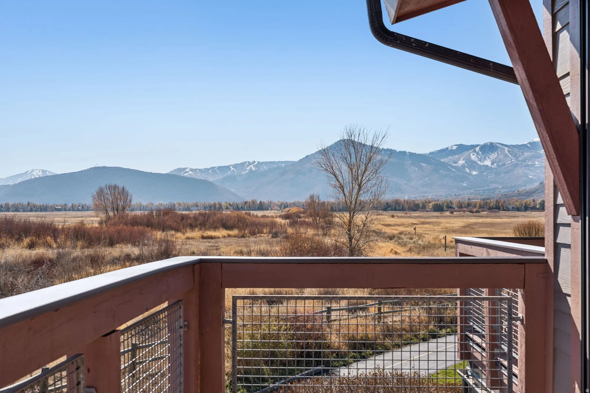 Expansive mountain and field scenery from a balcony with wood and mesh railing