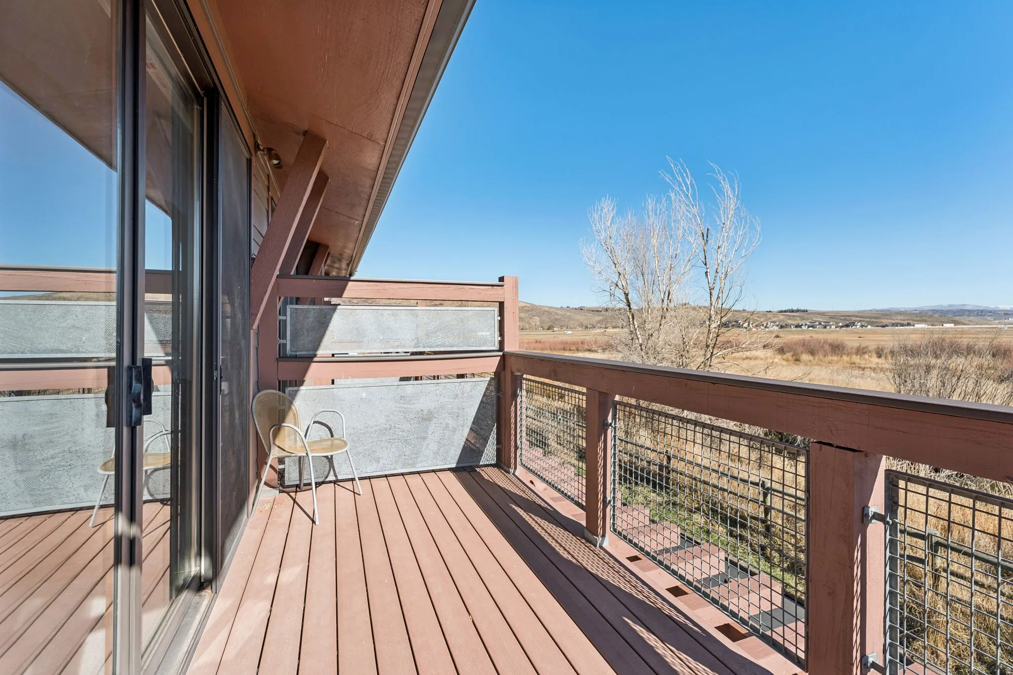 Expansive outdoor deck featuring wood-finish flooring, a wood and metal railing system, and a sliding glass door