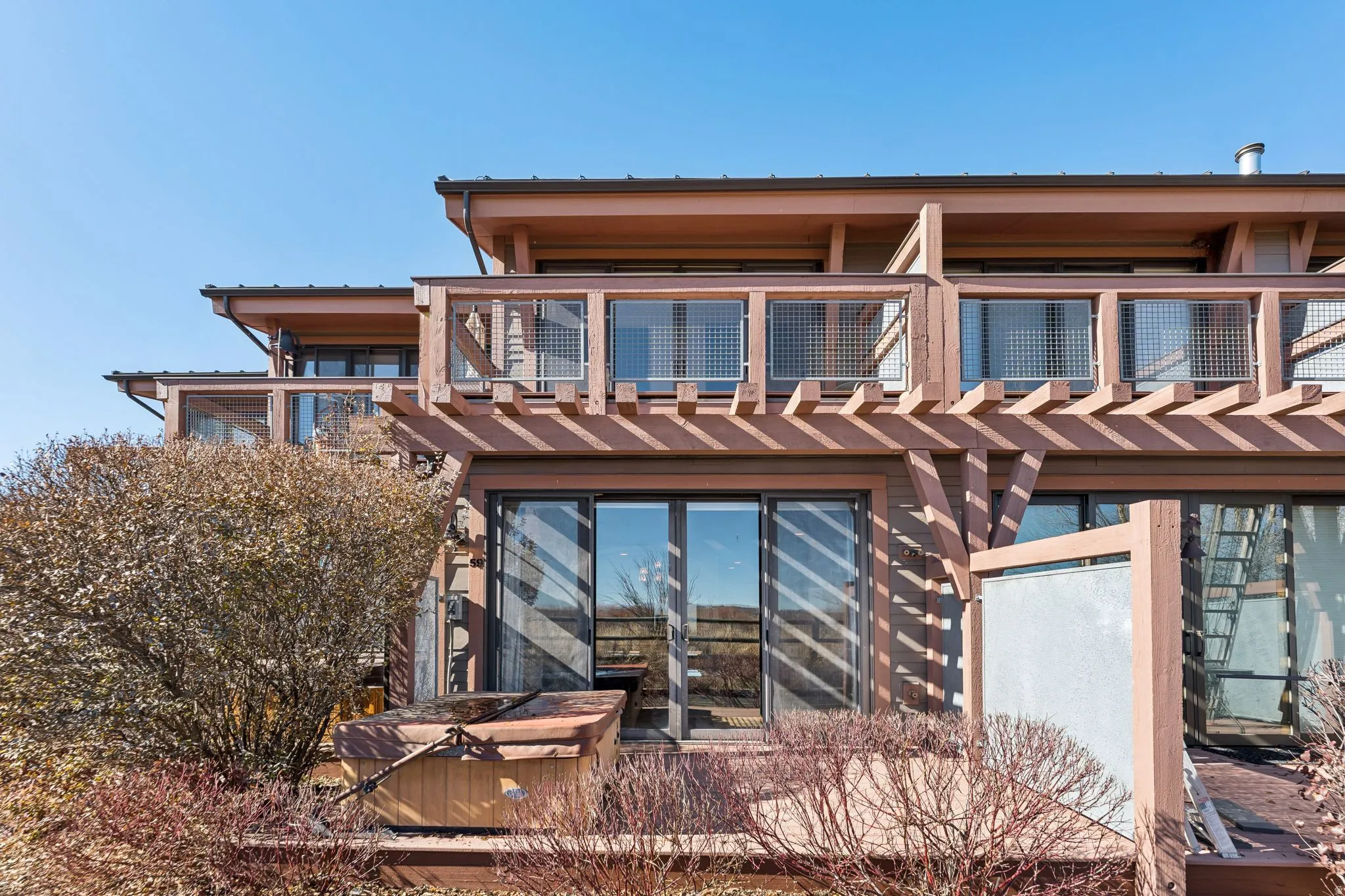 Multi-level exterior with multiple balconies, a wooden pergola, and sliding glass doors