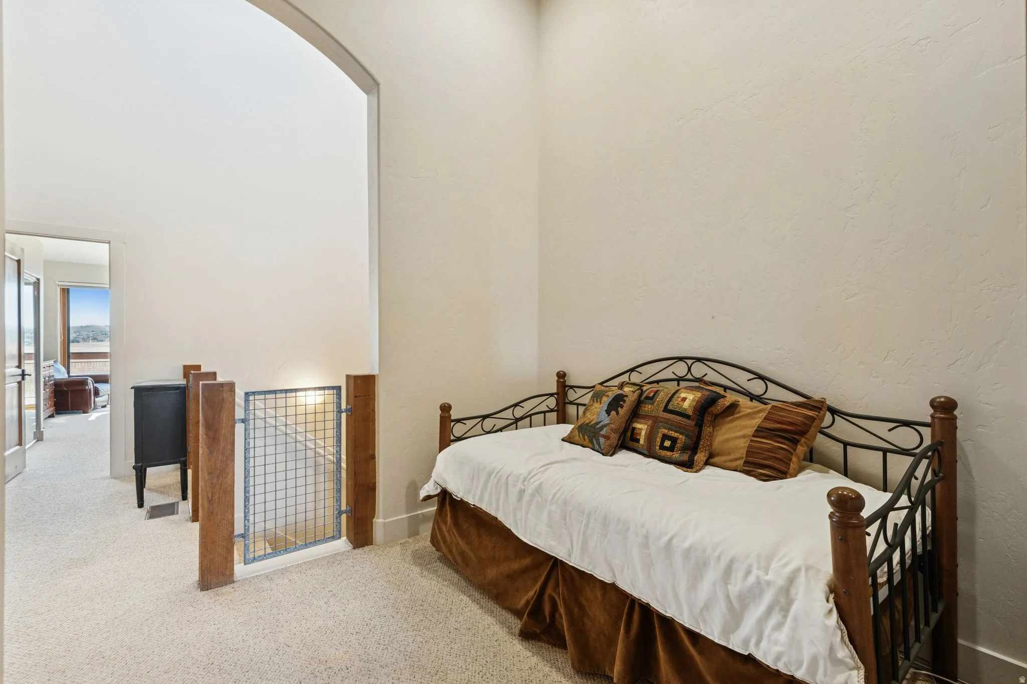 Carpeted loft area featuring an arched doorway, metal and wood-post staircase gate, and textured wall finish