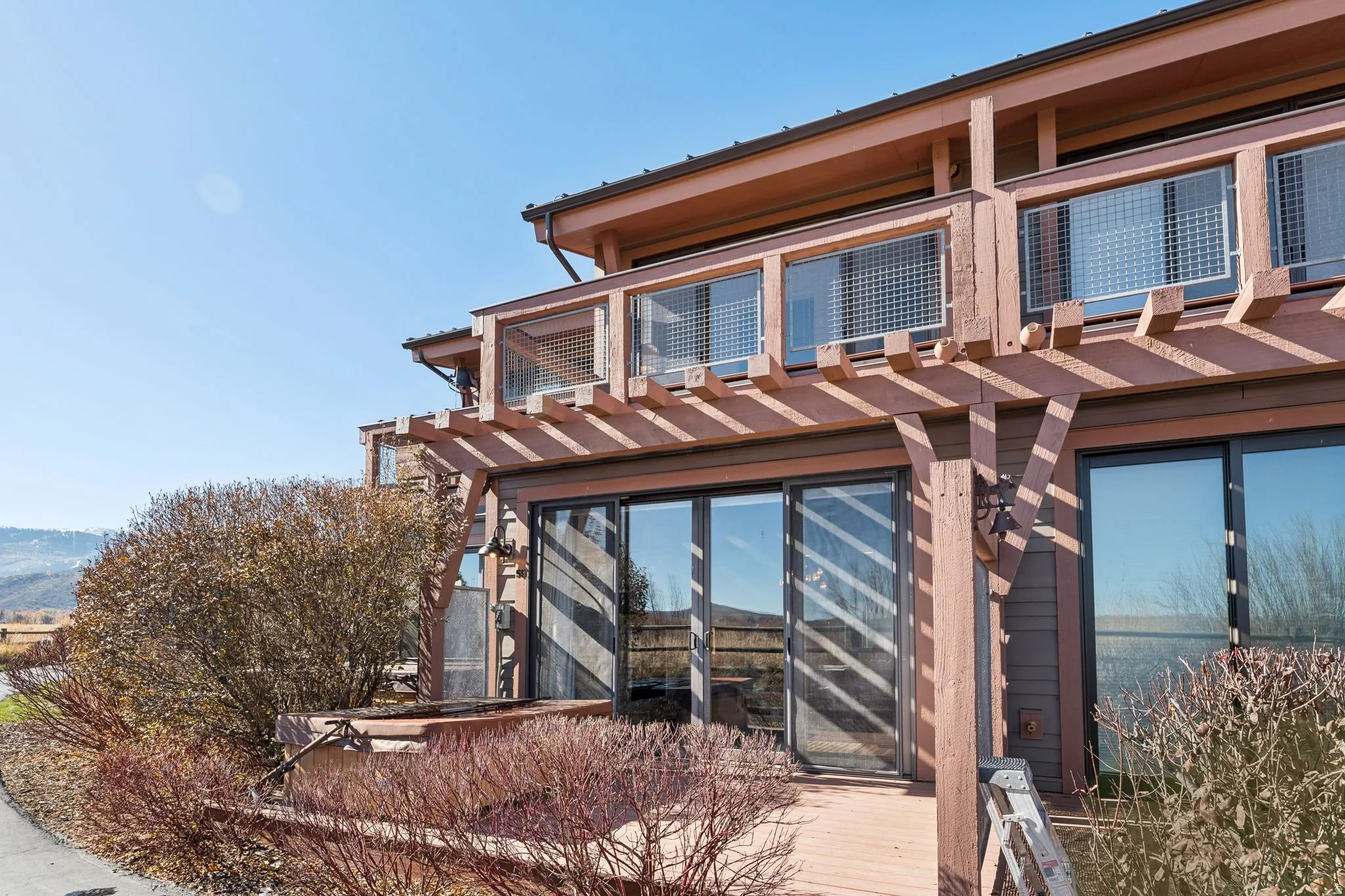 Multi-level exterior with a wood pergola, multiple sliding glass doors, and upper-level balconies featuring metal grate railings