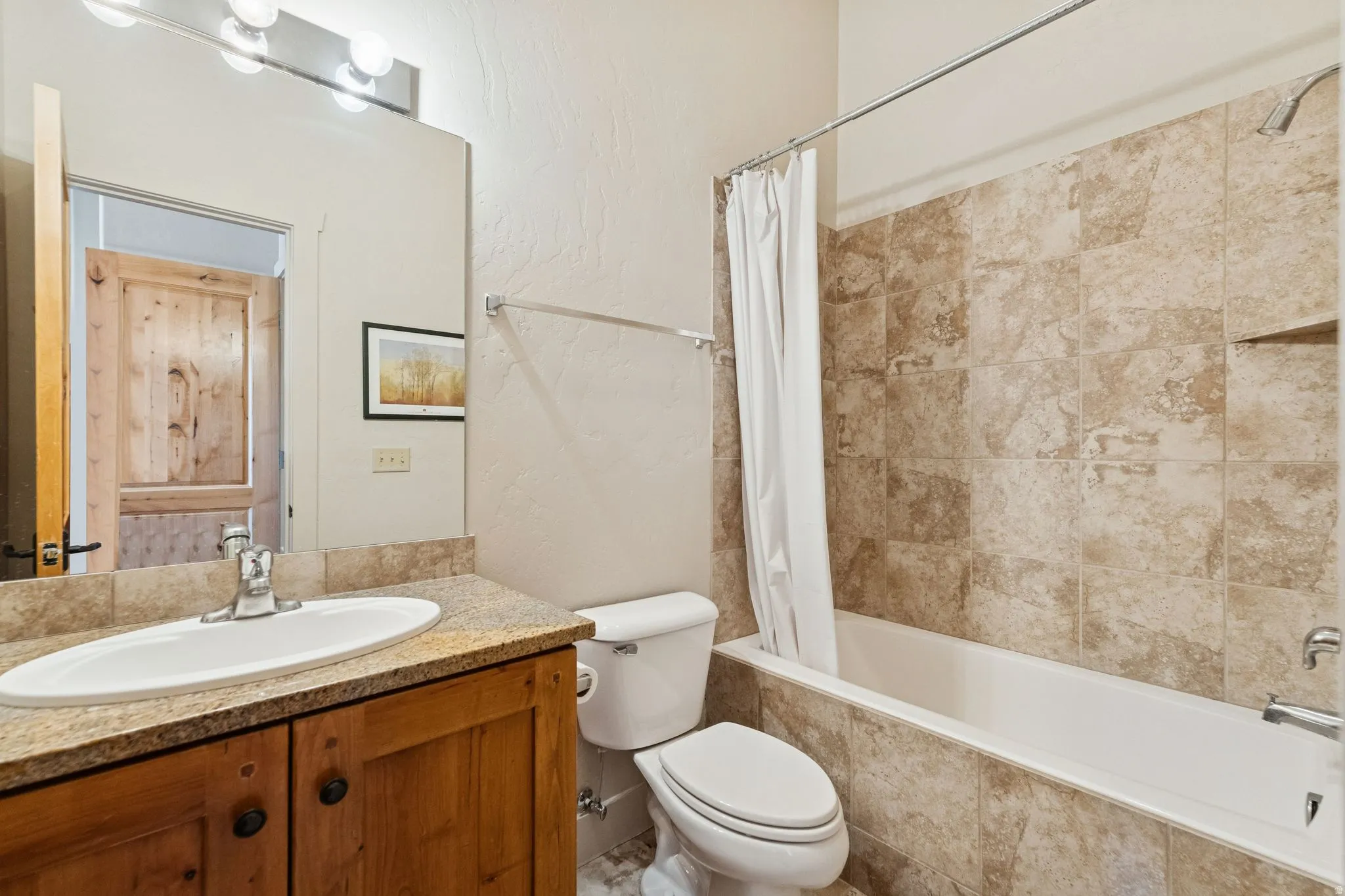 Bathroom featuring a wood-finish vanity with a drop-in sink, stone-finish countertop, and a tiled shower/tub combination with an integrated niche