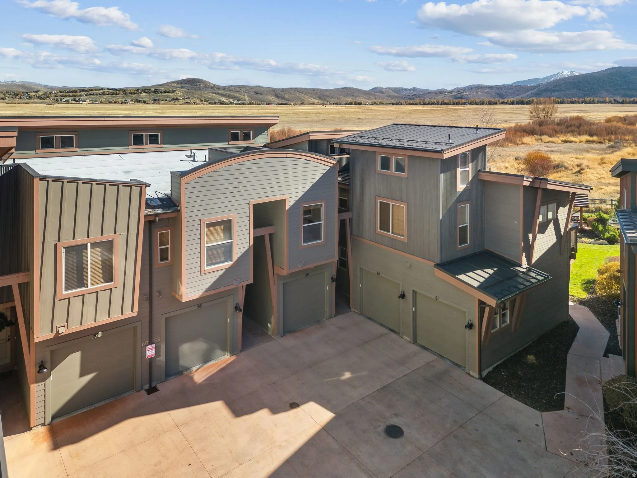 Contemporary multi-level townhome exteriors featuring varied siding textures, private garages, and a paved drive