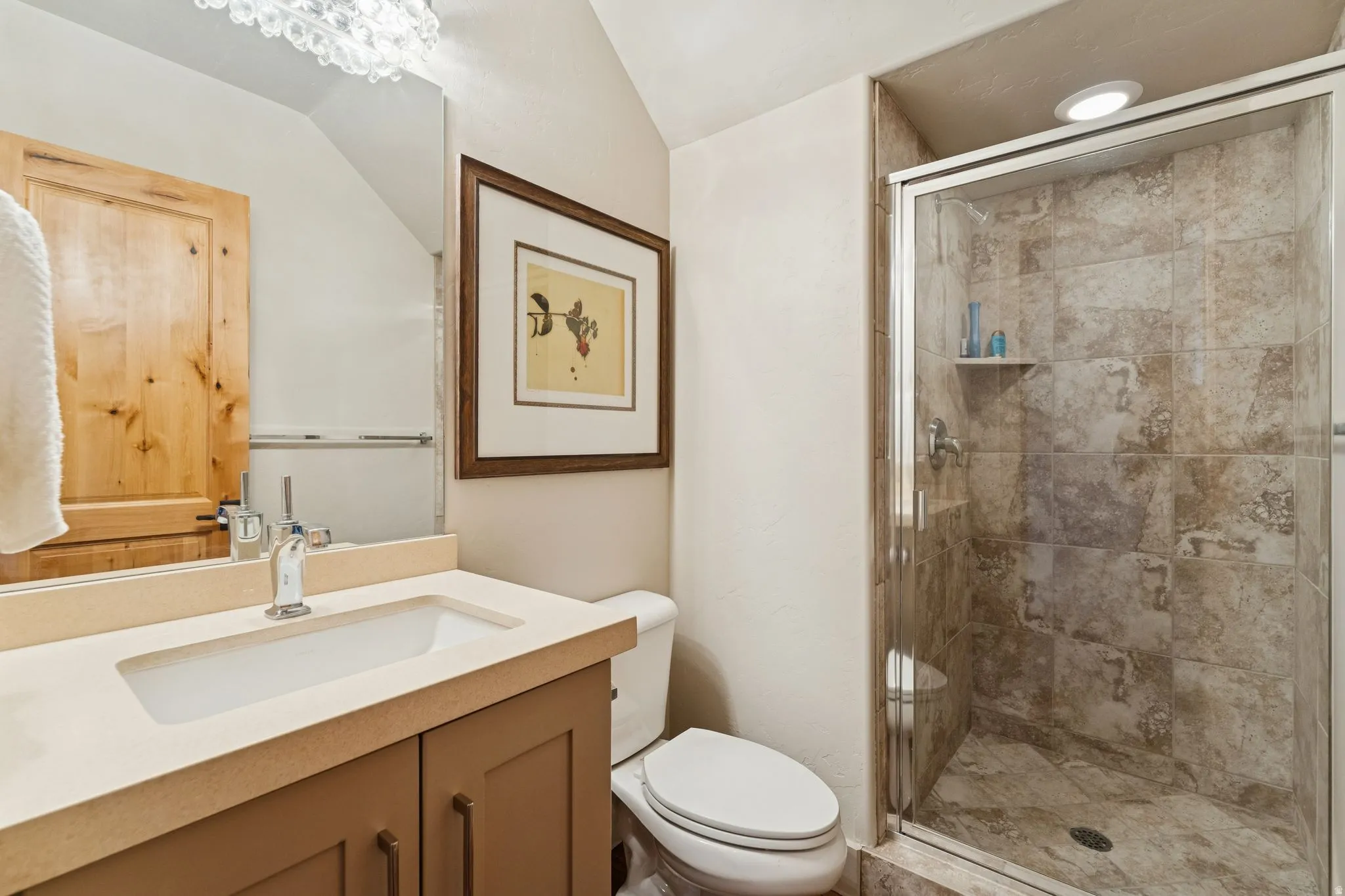 Bathroom featuring a walk-in shower with tile surround and glass enclosure, a single vanity with an integrated sink, a toilet, and a decorative light fixture