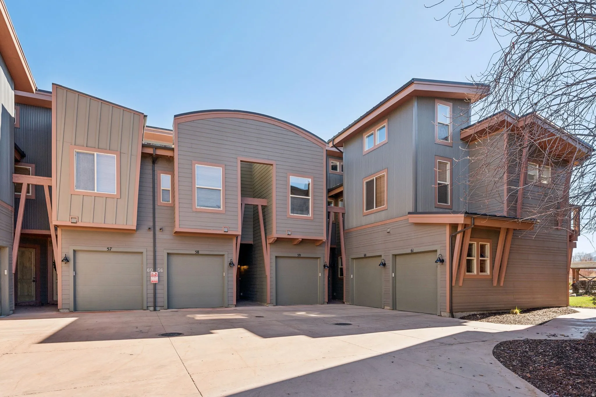 Multi-level townhome exterior featuring contemporary architectural design elements, varied siding materials, attached garages, and a paved driveway