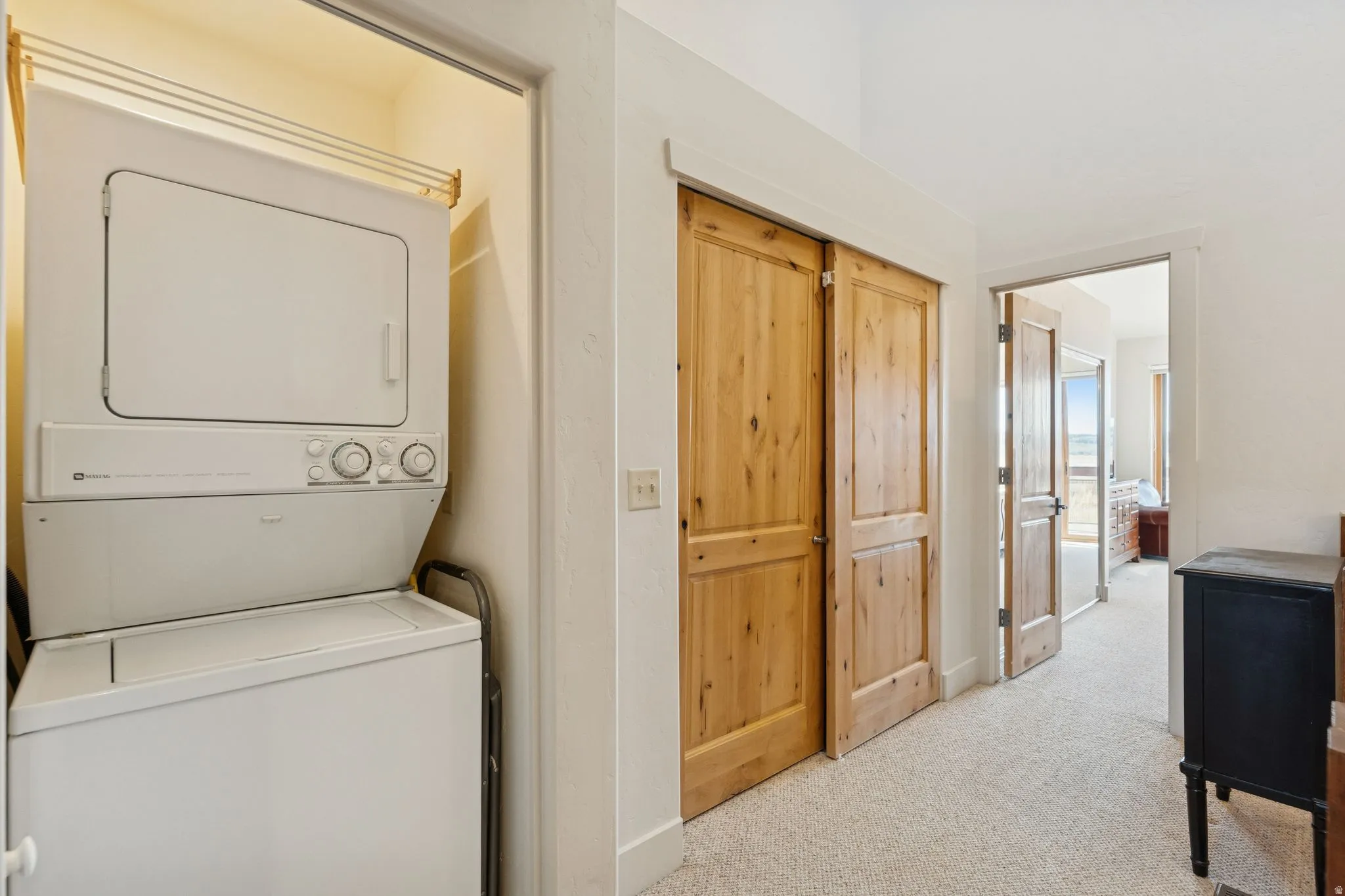 Dedicated laundry area with a stackable washer and dryer, adjacent to natural wood-finish closet doors and a carpeted hallway