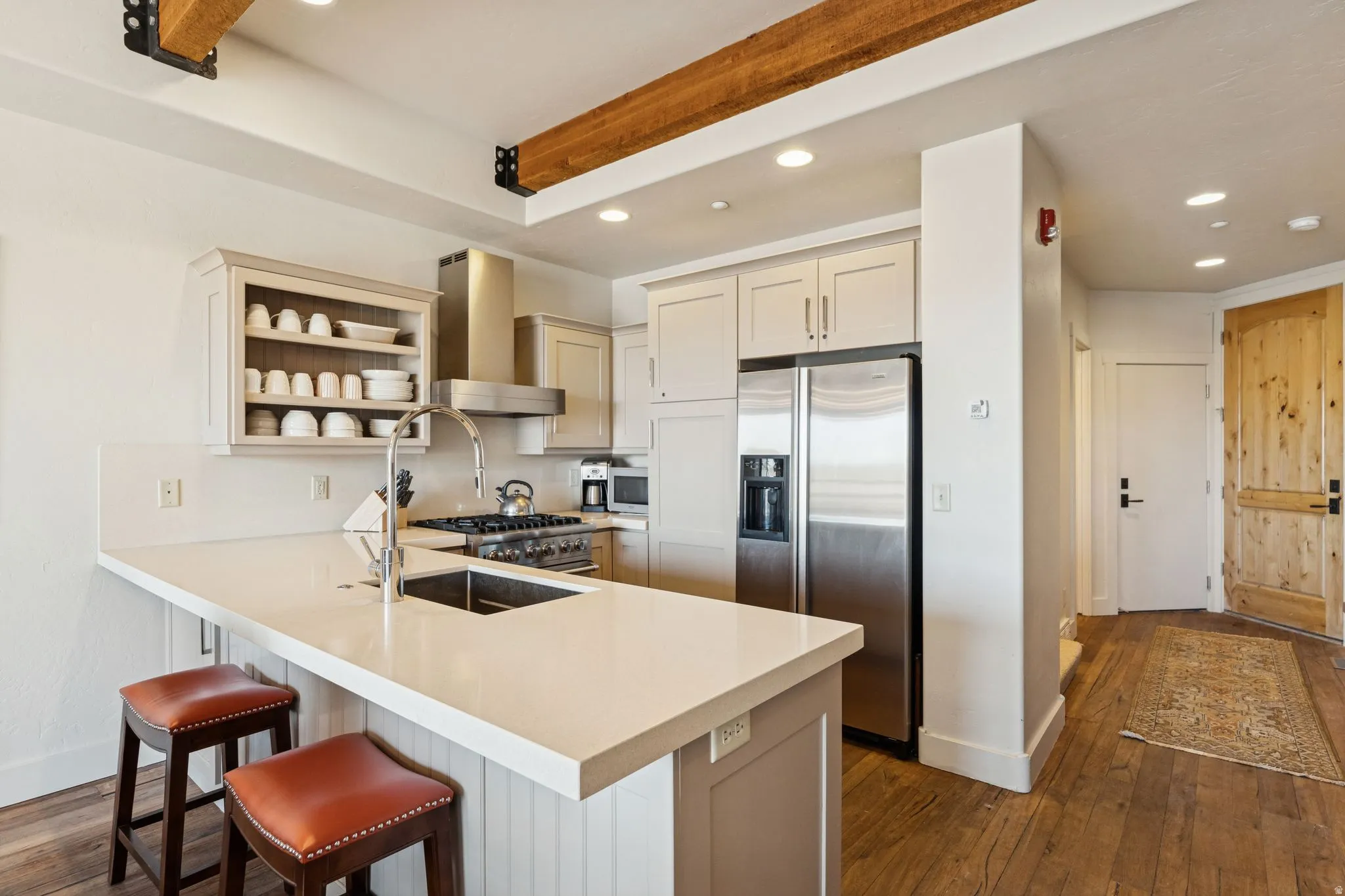 Kitchen featuring a peninsula with countertop seating, stainless steel appliances, wood-finish flooring, exposed wood beams, and recessed lighting