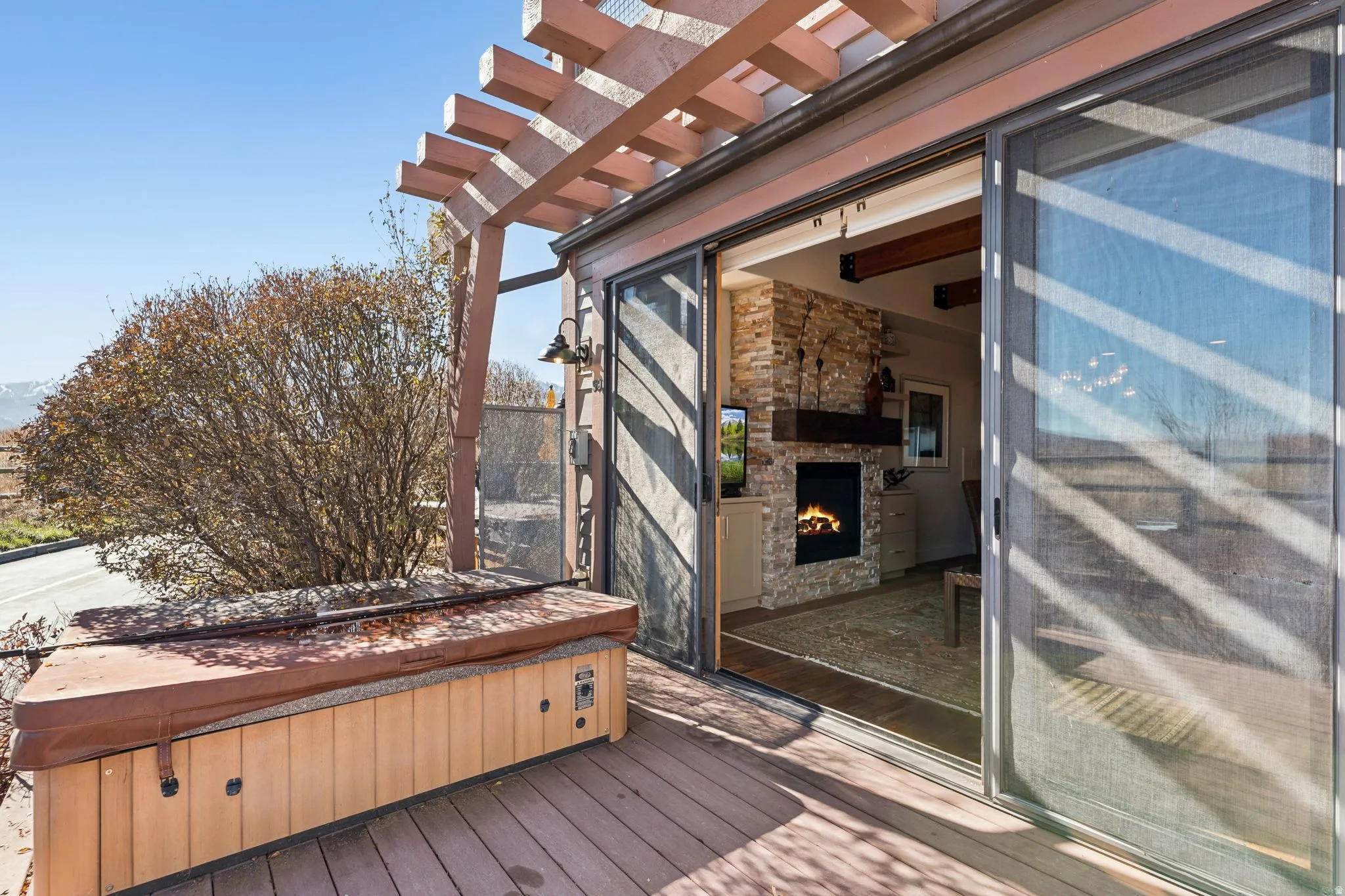 Spacious exterior deck with wood-finish flooring, featuring a built-in hot tub, and a wood pergola