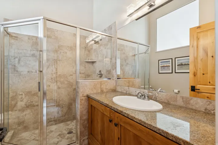 Bathroom featuring a glass-enclosed shower with full tile surround, a wood vanity with a stone countertop, an oval undermount sink, and a large mirror