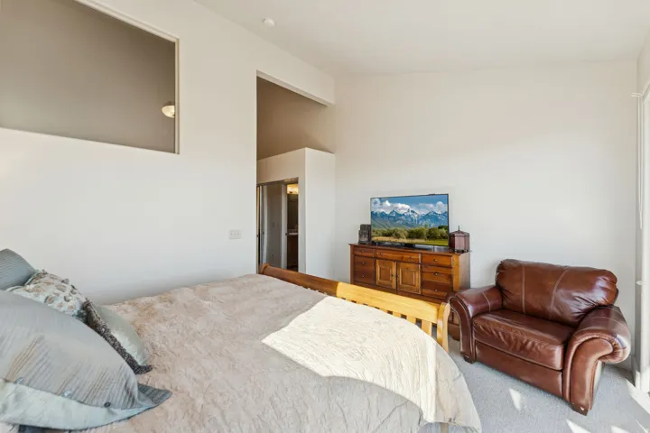 Bedroom featuring a wood-finish dresser, neutral carpeting, and high ceilings