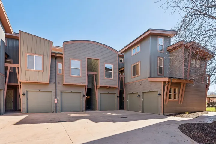 Multi-level townhome exterior featuring contemporary architectural design elements, varied siding materials, attached garages, and a paved driveway