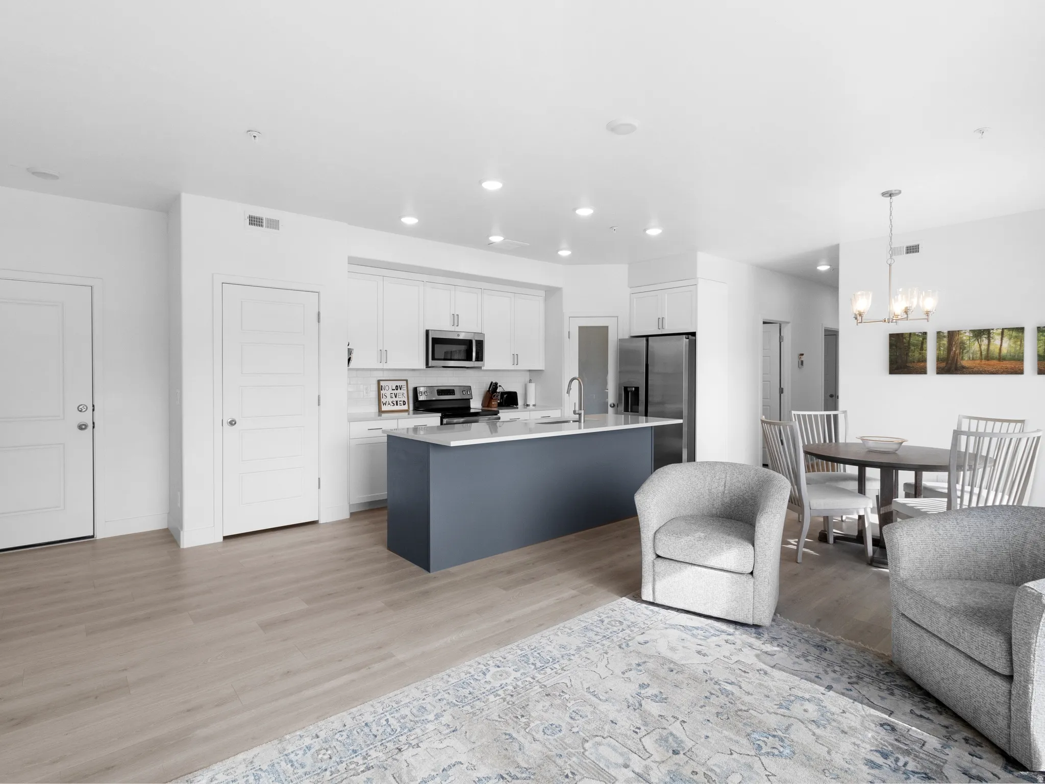 Dual tone kitchen featuring open floor plan, a kitchen island with sink, light wood-style flooring, stainless steel appliances, and two tone cabinets