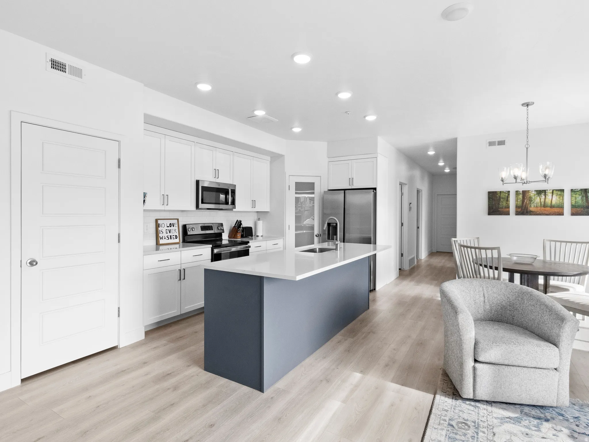 Dual tone kitchen featuring dual tone cabinets, an island with sink, stainless steel appliances, light wood finished floors, and suspended lighting