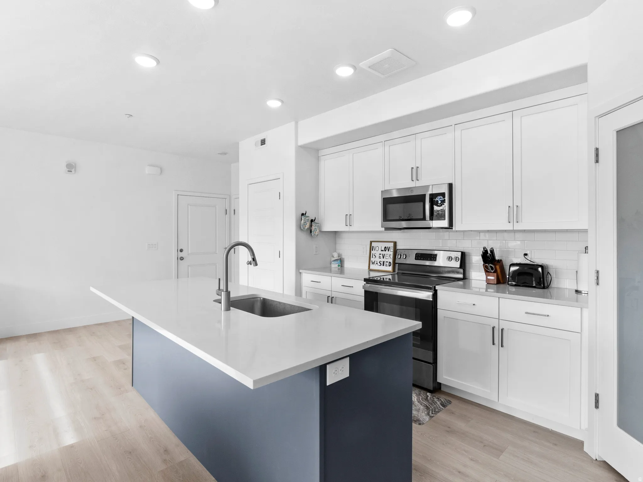 Kitchen featuring stainless steel appliances, dual tone cabinets, light wood-type flooring, an island with sink, and decorative backsplash