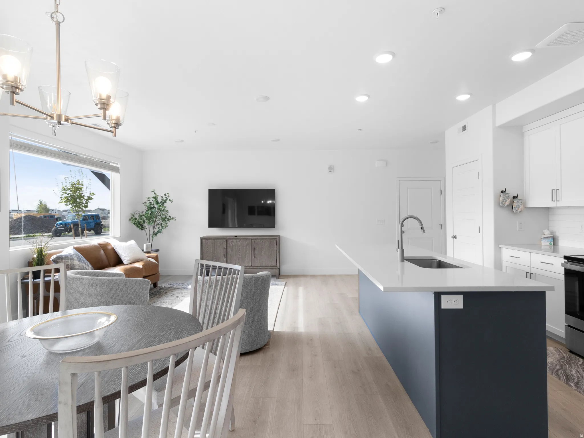 Dual tone kitchen featuring open floor plan, a center island with sink, dual tone cabinetry, light wood-type flooring, and a chandelier
