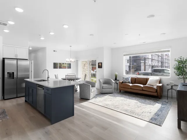 Kitchen featuring stainless steel appliances, two tone cabinets, open floor plan, an island with sink, and light stone counters