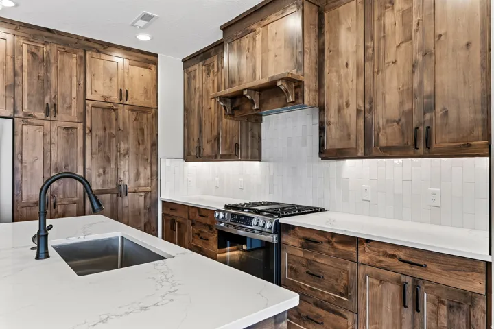 Kitchen featuring extensive wood cabinetry, white stone countertops, and a subway tile backsplash