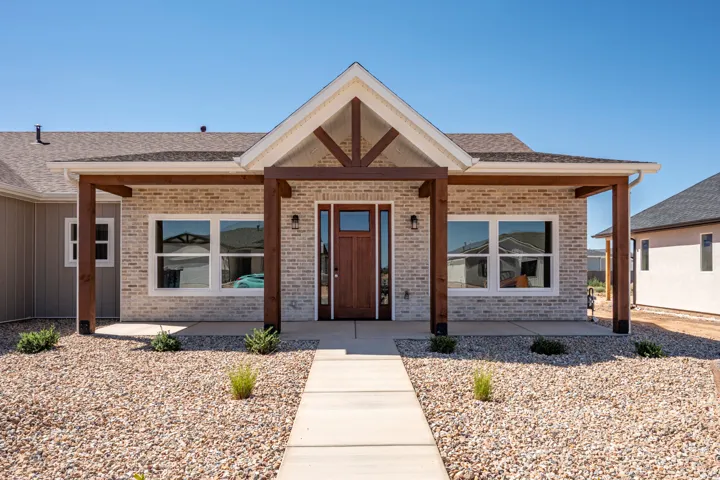 Contemporary exterior featuring light brick facade, dark wood-tone support beams, a solid wood-tone front door with glass sidelights, and a gravel-covered front yard with a concrete walkway