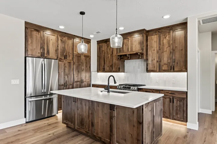 Kitchen featuring custom wood cabinetry, stainless steel appliances, a center island with a white stone-finish countertop, pendant lighting, and wood-finish flooring