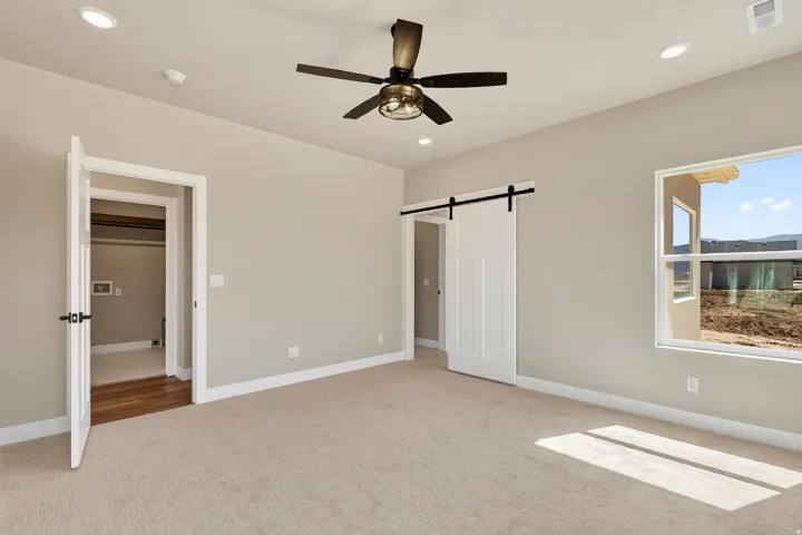 Spacious room featuring neutral carpeting, recessed lighting, a modern ceiling fan, a white barn door, and a large window