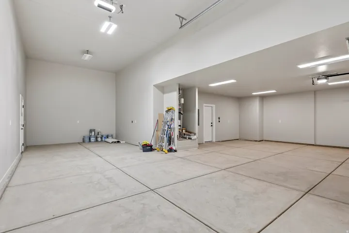 Spacious multi-car garage featuring a concrete floor, high ceilings, multiple overhead light fixtures, and a side entry door
