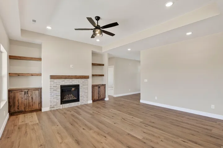 Living area featuring wood-finish flooring, a brick-surround fireplace with a wood mantle, built-in shelving, recessed lighting, and a ceiling fan