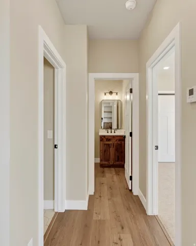 Hallway featuring wood-finish flooring, light neutral wall paint, and white trim