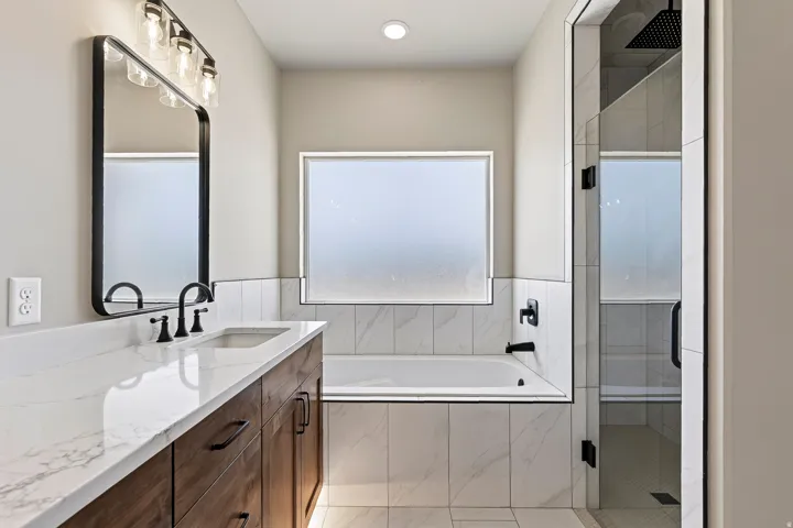 Bathroom featuring a wood-finish double vanity with a stone countertop, an undermount sink, and matte black fixtures