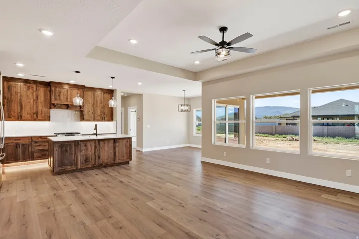 Open-concept living space featuring wood-finish flooring, a kitchen with distressed wood cabinetry, a central island with a light-toned countertop, a range, and pendant lighting