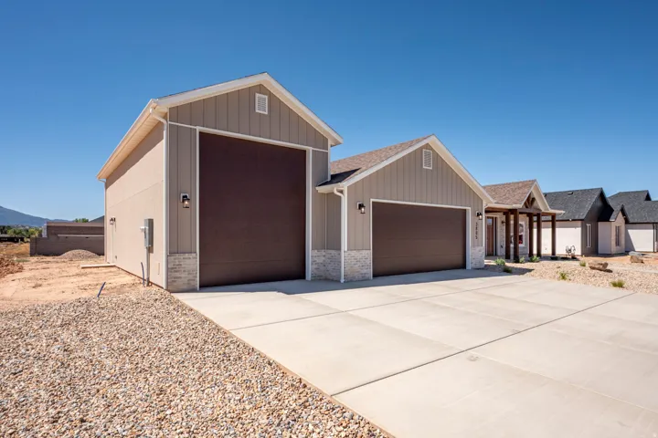 Contemporary exterior featuring a three-car garage, neutral-toned vertical siding, stone veneer accents, and a covered entry porch with timber columns