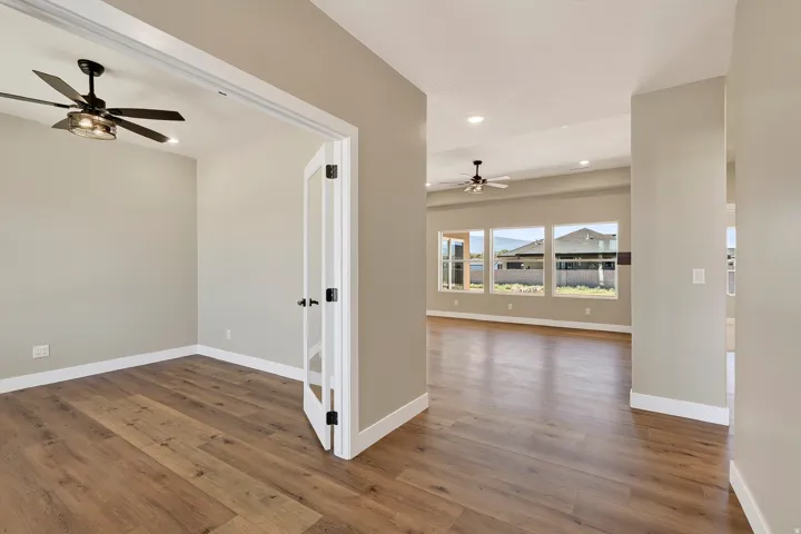 Double French doors open to a spacious room featuring wood-finish flooring, a ceiling fan with integrated lighting, and neutral wall tones